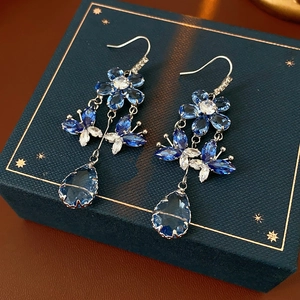 Detailed view of floral butterfly crystal earrings with water drop pendants on blue box