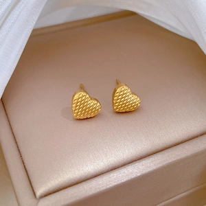 Close-up of golden heart-shaped stud earrings with quilted lattice texture on champagne silk