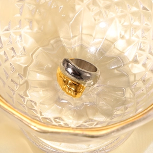 Polished silver and gold two-tone stainless steel crossover ring in a glass bowl