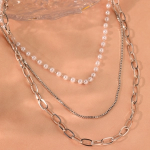Detailed close-up of a three-layer silver necklace with pearls and chunky oval links