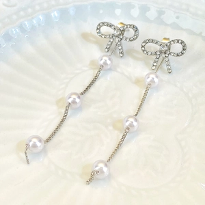 Close-up of elegant bow earrings with rhinestones, pearls, and long metal tassels