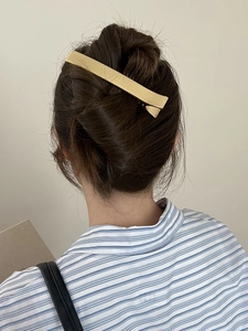 Détail d'une pince à cheveux rectangulaire en métal doré brossé sur un chignon