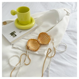 Detail view of golden shell clutch bag with pearl chain resting on white fabric background