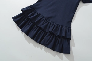 Détail d'une jupe en maille bleu foncé avec doubles volants sur un fond gris clair