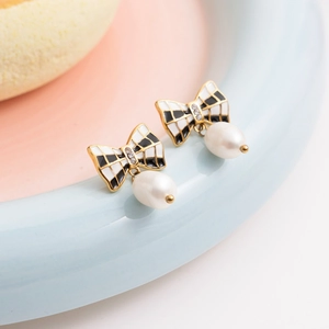 Macro detail of gold bow earrings with black and white enamel and white pearl drop