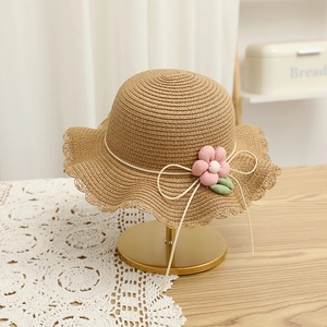 Detail of child straw hat with pink fabric flower and wavy brim on a golden stand