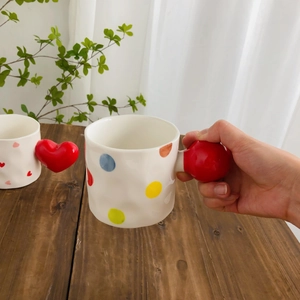 Detail of hand holding ceramic mug with colorful dots and a red heart-shaped handle