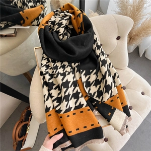 Thick houndstooth scarf with tassels in black, beige, and orange draped on a chair