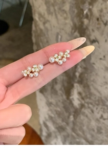 Detail of floral pearl stud earrings with green zircon accents held in hand