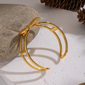 Détail d'un bracelet jonc doré avec nœud papillon posé sur un socle en pierre naturelle