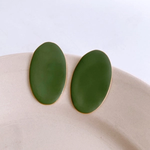Detail of dark olive green oval enamel earrings with gold trim on a beige ceramic plate