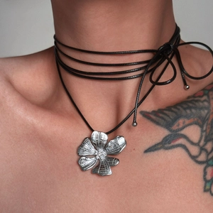 Detail of multi-strand black cord choker featuring a textured silver flower pendant
