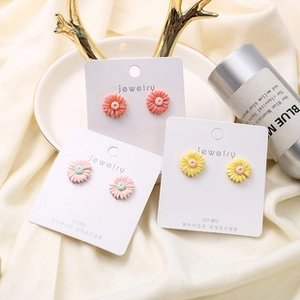 Macro detail of three pairs of daisy stud earrings in pink, yellow, and coral resin