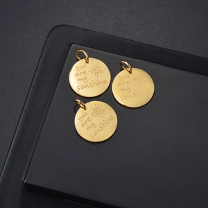 Vue macro de trois pendentifs soleil dorés en acier inoxydable avec gravure You Are My Sunshine