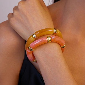 Gros plan de bracelets géométriques en résine ambre et rose corail avec anneaux en or