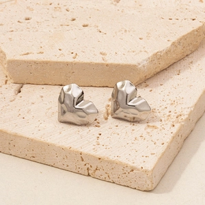 Macro shot of silver heart stud earrings with geometric facets on a stone surface