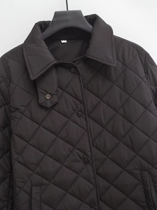 Front view of black quilted jacket hanging on hanger with collar and snap buttons