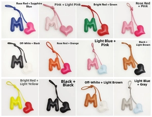 Detail view of M-letter heart bag charms in 12 assorted colors with contrast stitching
