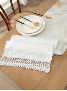 Close-up of white table runner featuring elegant leaf jacquard patterns and tassel edges