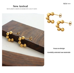 Close-up of golden C-shaped bead earrings with six polished balls on a wooden base