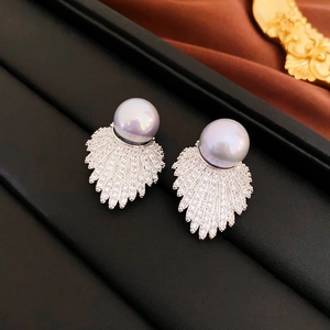 Macro shot of faux pearl earrings with fan shaped zircon leaves on black leather