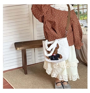 Close-up of white quilted crossbody bag with a cute 3D brown plush bear decoration