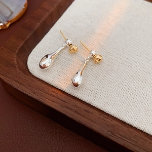 Detail shot of teardrop metal earrings in silver and gold on a textured wooden tray