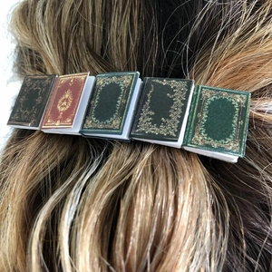 Close-up of miniature vintage book hair clip with gold patterns on colorful covers