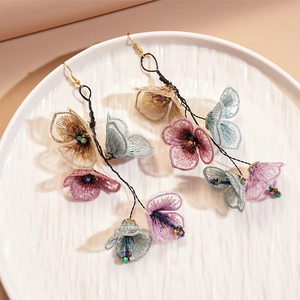Elegant floral tassel earrings with embroidered petals and glass beads on a ceramic plate