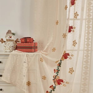 Detail of Christmas beige lace curtain with red bell and snowflake embroidery