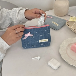 Detail of denim coin purse with white embroidery and pink satin bow on a white desk