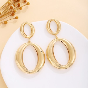 Detail of elegant gold oval drop earrings on a white stand with dry floral decor