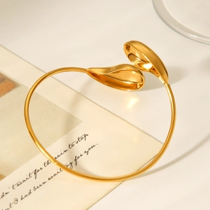 Macro detail of high-polish 18k gold teardrop-shaped open bangle on an aesthetic background