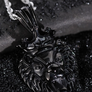 Detail shot of a black stainless steel roaring lion head pendant with crown on textured sand