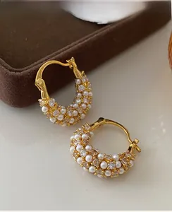 Detailed close-up of gold plated C-shaped earrings with pearls and zircons on velvet