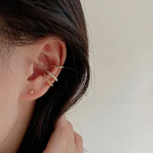 Détail de trois bagues d'oreille dorées avec anneau poli, strass et texture torsadée