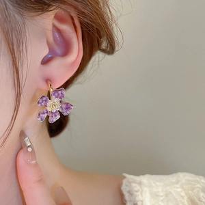 Close-up of a model wearing a purple crystal flower C-shaped earring in a warm setting