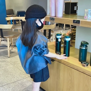 Primer plano de niña con camisa azul de manga corta y gorro de punto en una cafetería