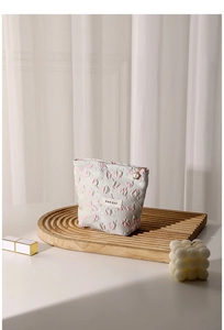 Floral embossed gray fabric makeup bag on a wooden tray with a lipstick and candle
