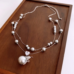 Gros plan du collier de perles double épaisseur avec zircon cœur et pendentif nœud en bois