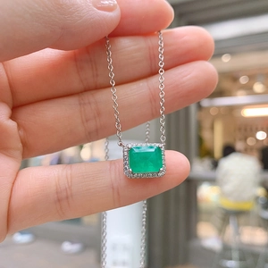 Close-up of a silver necklace featuring a square green zircon pendant with halo setting