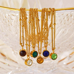 Six colors of 18K gold plated stainless steel birthstone necklaces on glass bowl edge