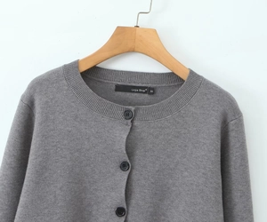 Detail of grey knitted cardigan with round neck and black buttons on a wooden hanger