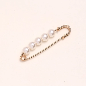 Macro shot of 5 white pearls on a gold safety pin for waist adjustment and fashion detail