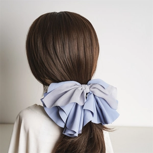 Blue and grey large fabric bow hair clip worn by a model against a white background