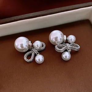 Elegant bow-knot pearl earrings in silver finish on a premium leather background