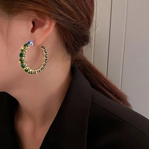 Primer plano de modelo con pendientes de aro dorados y piedras de circón verde esmeralda