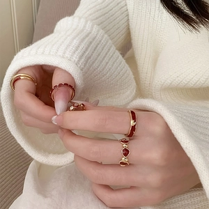 Close-up of gold flower and heart rings with red enamel finish on a model's hand