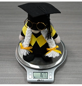 Detail shot of a graduation gnome with glasses on a scale showing 167.1g weight