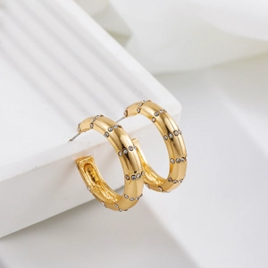 Détail macro de boucles d'oreilles en C plaquées or 18 carats avec strass incrustés